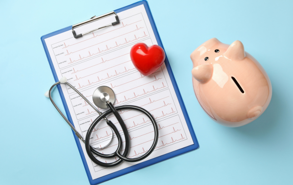 Illustration of a clipboard with a piggy bank to the right, and a stethoscope and a red heart laying on top of the clipboard