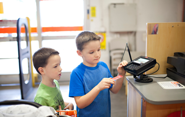 Two children are in a store. One child is about to insert his debit card into the POS machine to make a payment