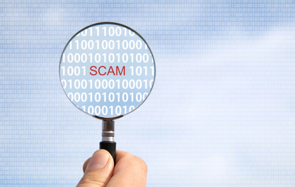 A person holds a magnifying glass. In the glass, you see the word "SCAM" in red letters, surrounded by zeroes and ones